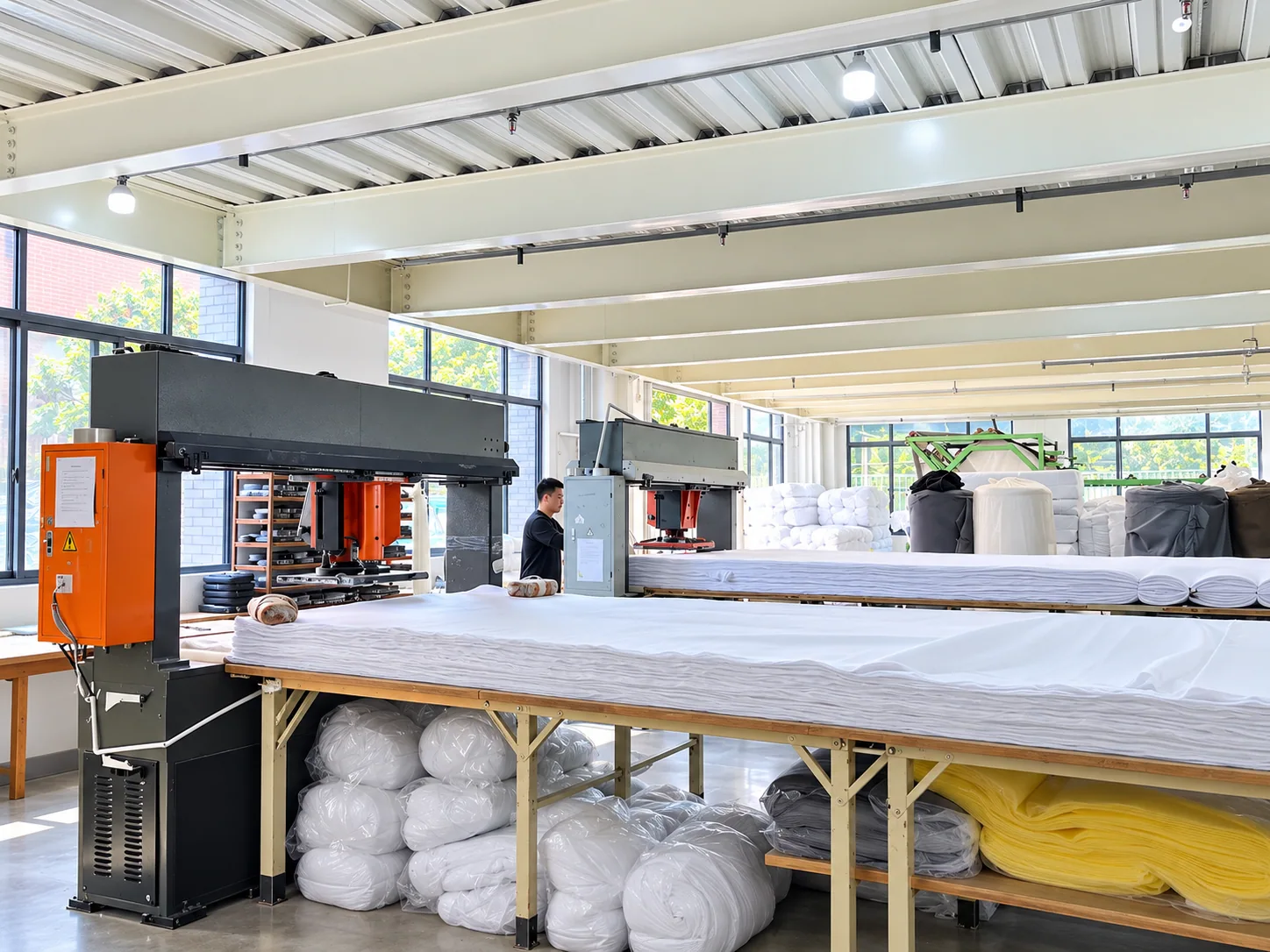 Cutting equipment beside tables of layered white fabric in a workshop